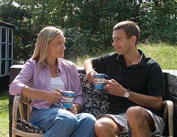 Par drikker kaffe i solen ved sommerhus